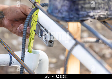 Plumber Using Level And Tape Measure While Installing PVC Pipe At Construction Site. Stock Photo