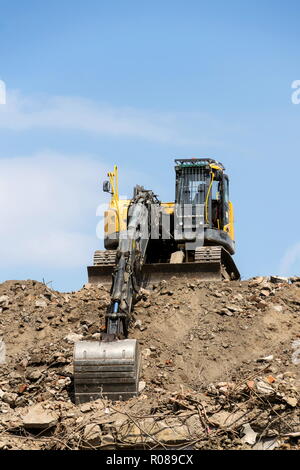 Yellow construction digger, excavator on demolition site stand on debris, sunny day clear blue sky Stock Photo
