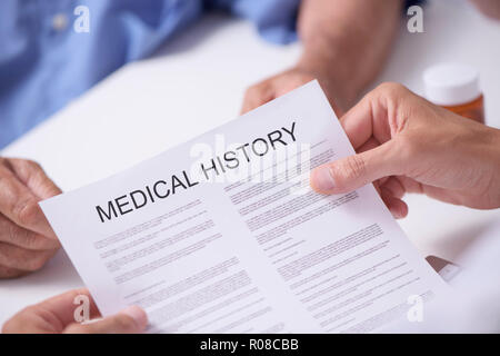 closeup of a caucasian doctor man reading the medical history of a senior caucasian patient man, sitting both at the doctors desk Stock Photo