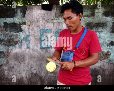 ANTIPOLO CITY, PHILIPPINES - OCTOBER 27, 2018: A street vendor slices a ripe pineapple which he sells on a sidewalk. Stock Photo