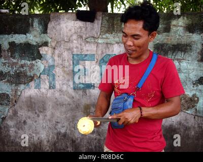 ANTIPOLO CITY, PHILIPPINES - OCTOBER 27, 2018: A street vendor slices a ripe pineapple which he sells on a sidewalk. Stock Photo