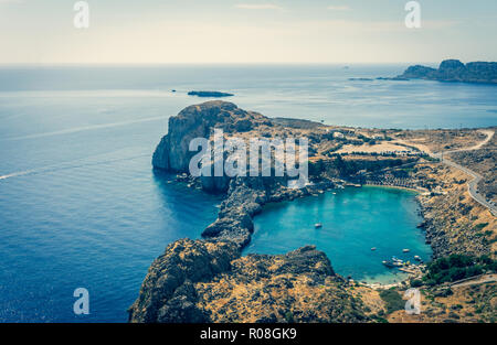 Vintage horizontal photo with nice cove on Rhodes island. Cove is captured from ancient acropolis above the Lindos town. Several sunbeds are visible i Stock Photo