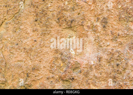Horizontal photo with wall texture. Wall is covered by plaster which is worn and cracked. Several dark stones are placed on wall with send grains. Col Stock Photo