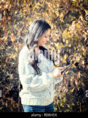 Beautiful Young Hispanic, American Indian, Multi-racial Woman Checking Messages & Taking Selfies with Cell Phone Outside on a Fall Day Stock Photo