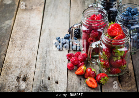 Berries in glass jars - homemade jam, smoothie, low fat dessert, rustic wood background Stock Photo