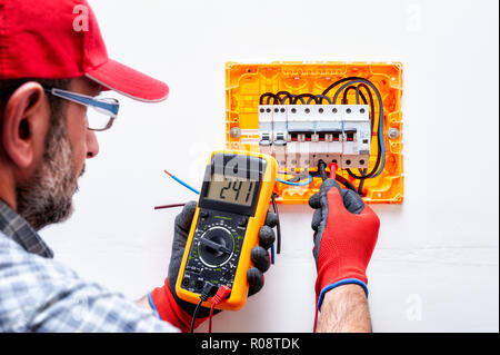Electrician technician with gloves protected hands, measures the voltage in a residential electrical panel. Stock Photo