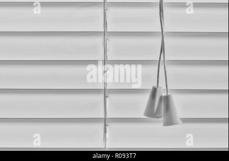 A pair of Venetian blind pull strings cast in shadow with white blinds behind them, creating negative space with horizontals with an abstract look. Stock Photo