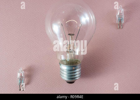 Two G4 bipin halogen lamps and a tungsten filament bulb arranged diagonally on a pink background showing technology going obsolete Stock Photo