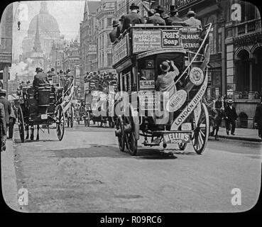 Late 19th century Victorian black and white photograph taken on the streets of London, showing horse drawn omnibuses, covered on adverts,  carrying many passengers, plus street crowded with people. Shop signs are also visible. Stock Photo