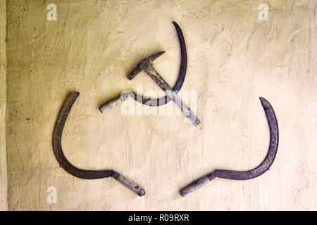 Old garden tools used to decorate a garden wall, including the hammer and sickle emblem of the Communist Party and the Soviet Union (USSR) Stock Photo