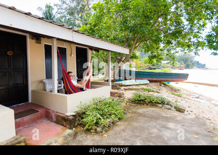 Young tourist relaxing on hammock on hotel balcony on tropical Tioman island in Malaysia. Beautiful resort in south east asia on Tekek beach. Stock Photo