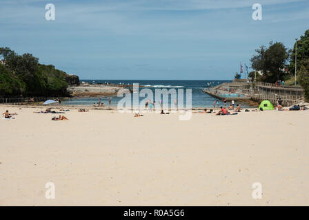 View of the golden sands of Clovelly Beach, Sydney, with people sunbathing and swimming in  the sea and to the right a swimming pool. Stock Photo