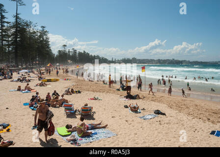 View along the golden sands of Manly Beach, Sydney, Australia with holidaymakers sunbathing, swimming and surfing in the spring sunshine. Stock Photo