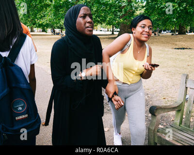 Indian and black student girls walking in a park holding by the hand with a mobile phone in her hand Stock Photo