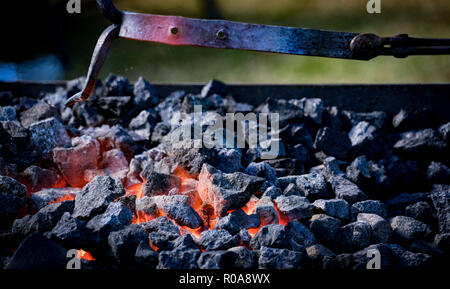 A blacksmith heating up iron in a bed of glowing hot coals, casting a brilliant orange light inside the traditional forge. Stock Photo
