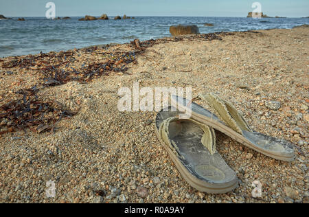 Symbol of peace and solitude: pair of worn and worn slippers abandoned on the seashore. Stock Photo