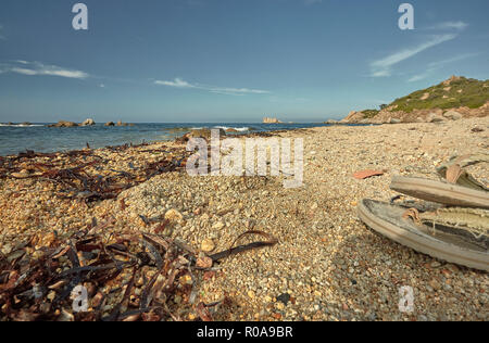 Detail of a Mediterranean beach during the summer with a pair of flip-flops sprouting on the right side of the image. Stock Photo