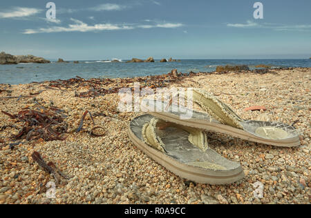 Conceptual image symbol of loneliness and relaxation containing a pair of old and worn slippers resting on the sand of a paradisiacal beach with the s Stock Photo