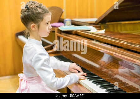 A girl in a beautiful dress plays on a brown grand piano Stock Photo