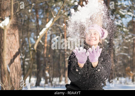 Girl throws snow up. Portrait of the beautiful girl throwing snow in the winter. Happy young woman plays with a snow in sunny winter day. Stock Photo