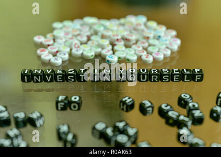 INVEST IN YOURSELF  written with Acrylic Black cube with white Alphabet Beads on the Glass Background Stock Photo