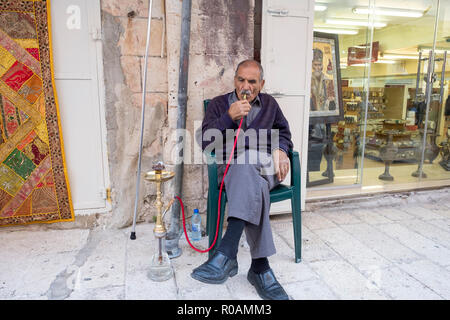 An Arabic man smoking a hookah outside of his shop  in the Muslim Quarter of the Old City of Jerusalem in Israel Stock Photo
