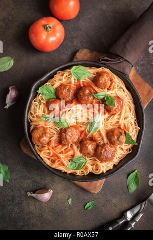 Spaghetti pasta with meatballs, tomato sauce and fresh basil in cast iron pan. Healthy homemade italian pasta on rustic background with copy space. Stock Photo