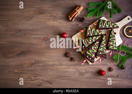 Chocolate Brownies in shape of Christmas Trees with green icing and festive sprinkles on wooden table, top view, copy space. Sweet homemade Christmas  Stock Photo