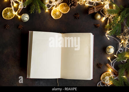 Christmas background with vintage blank open book, decor, lights and fir branches around on dark table, top view. Layout with empty copy space for tex Stock Photo