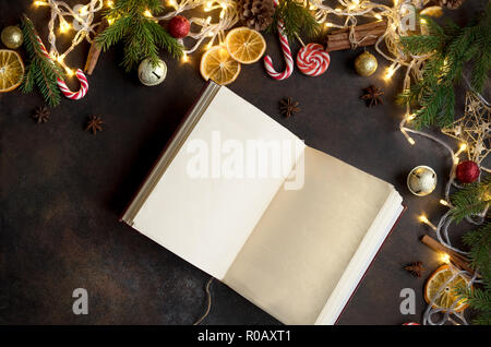 Christmas background with vintage blank open book, decor, lights and fir branches around on dark table, top view. Layout with empty copy space for tex Stock Photo