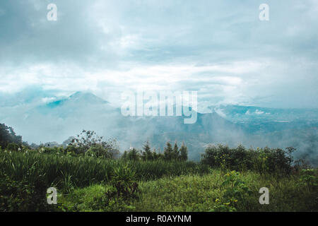 Panoramic of a grassy field with views over the green hilly landscape worked into small farms in the rural mountains of Guatemala Stock Photo