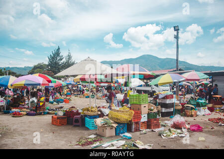 Vibrant food market stalls laid out on the floor by women in traditional Mayan dress under colorful parasol umbrellas in Antigua, Guatemala Stock Photo