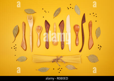 Handcrafted wooden utensils, pasta and spices on bright yellow background. Stock Photo