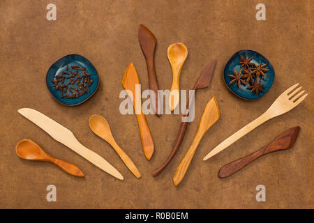 Handcrafted wooden utensils and spices on brown leather background. Fork, spoons and knives. Cloves and anise. Stock Photo