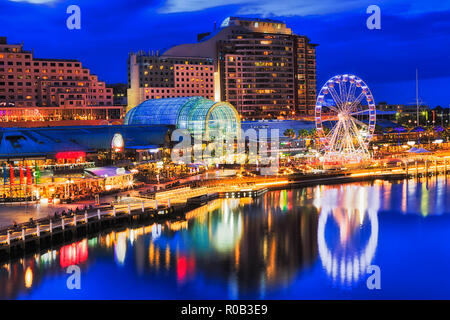 Ferries wheel on waterfront of Sydney Darling Harbour and harbourside entertainment area with boardwalks, cafes, hotels and accommodation at sunset wi Stock Photo