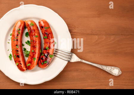 A closeup photo of a plate of fried sausages, shot from the top on a dark rustic wooden background with a fork and a place for text Stock Photo