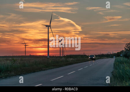 Wind turbines generating electricity next to a road at sunset, with a gorgeous cloudscape behind them Stock Photo
