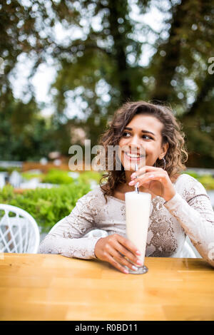 young beautiful woman sitting in a cafe drinking a milkshake and reading a book Stock Photo