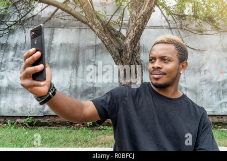 Close up of dark-skinned man in black T-shirt making selfie on mobile phone. Stock Photo