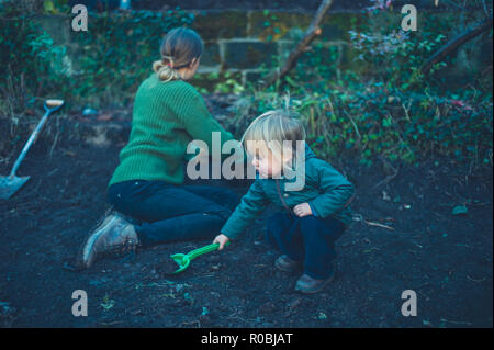 A mother and toddler are digging holes in the garden in the autumn Stock Photo