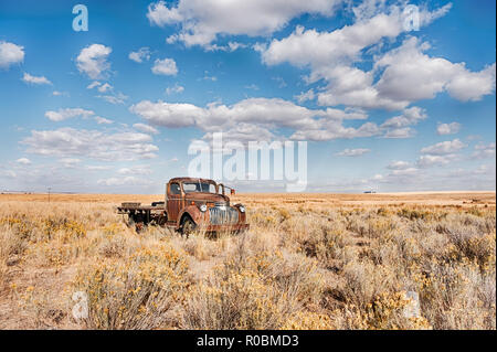 An old abandoned red truck sits in a field underneath a big blue sky with scattered clouds in Eastern Washington. Stock Photo