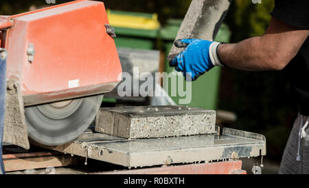 Building contractor working with a concrete block and an angle grinder, closeup view of his hands and the power tool. Stock Photo