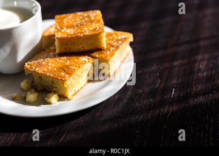 Close-up view of fresh baked corn bread with cheese and cup of yogurt in white plate on wooden table Stock Photo