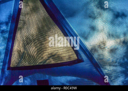 Tent interior looking outwards through screening material towards setting sun, with trees throwing leaf shadows on tent side. Good fabric texture. Stock Photo