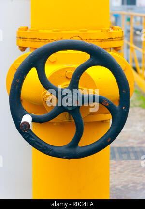 Large black manual handwheel in a control valve on a bright yellow pipe Stock Photo