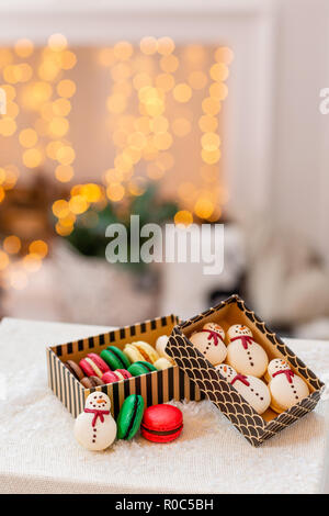 Variety of sweet macaroons in carton box. Cookie in the form of a snowman. Merry Christmas card. New year mood. lights of garland bulbs Stock Photo