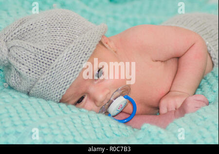 4 weeks old newborn baby boy with gray hat on green blanket with dummy in his mouth Stock Photo