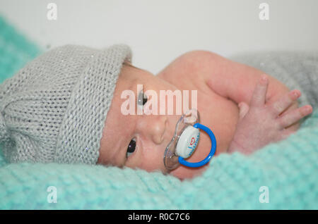 4 weeks old newborn baby boy with gray hat on green blanket with dummy in his mouth Stock Photo