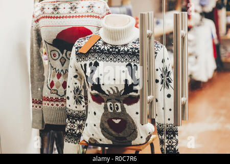 Christmas sweaters with reindeer and owl in window of shop in european city street. Christmas shopping and sales. Black friday sale. Festive decoratio Stock Photo