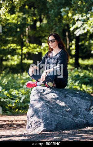 Middle age redhead caucasian woman sitting on a rock in lotus position in the forest Stock Photo